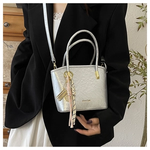 Detail of silver metallic bucket bag featuring golden charms and a branded logo