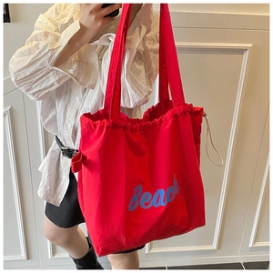Detail of red canvas tote bag with blue Beach text and drawstring closure on a model