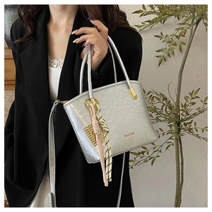 Detail of silver metallic bucket bag featuring golden hardware and woven charm