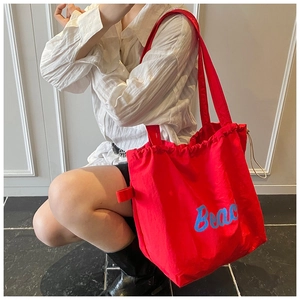 Close-up of bright red drawstring tote bag with blue Beach text worn by a model