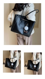 Close-up of black leather tote bag with a white plush smile charm and shoulder strap