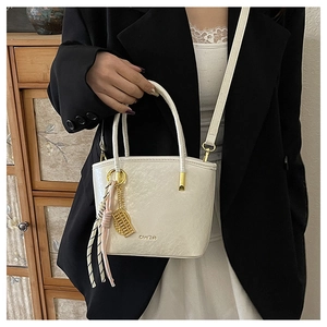 Detail of white textured PU leather bucket bag with brand logo and woven strap decoration