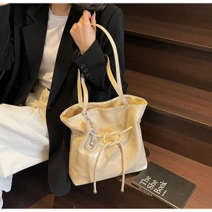 Dettaglio borsa tote beige con trama in pelle e ciondolo con perle e fiocco elegante