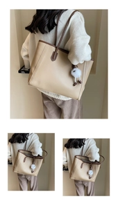 Detailed close-up of a large beige tote bag with brown trim and cute fuzzy charm