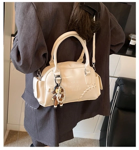 Detail of a retro cream leather bowling bag featuring side stitching and a bear pendant