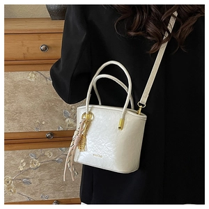 Macro detail of creamy white pleated PU bucket bag with gold lettering on a suit