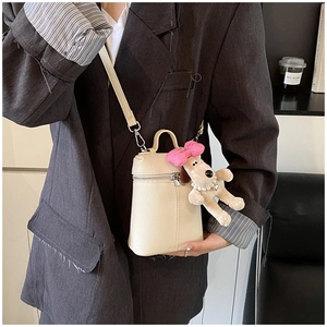 Detail of cream bucket bag in lychee leather featuring a plush dog charm and crossbody strap