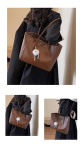 Detail of caramel leather tote bag with fine stitching and a white plush charm
