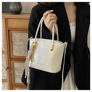 Detail of white PU bucket bag with leather texture, gold logo, and pink silk scarf accessory