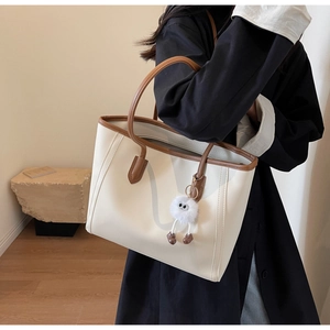 Detail of cream tote bag with brown leather handles and a cute plush toy pendant