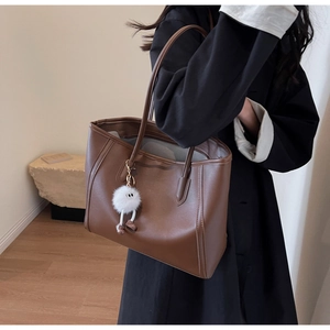 Detail of dark coffee tote bag with a white plush monster charm on matte leather