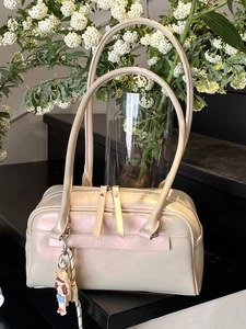 Elegant pearl white Boston bag with long handles and a cute pendant on a stone step