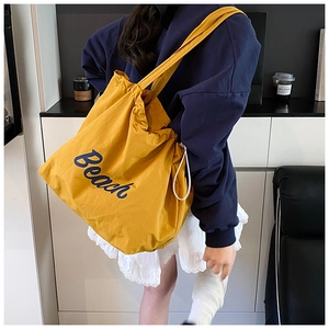 Detailed close-up of a large yellow canvas tote bag featuring blue Beach lettering print