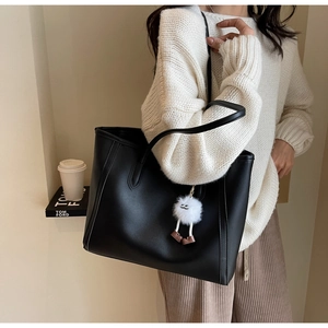Detail of a black leather tote bag with a white plush charm shown on a model