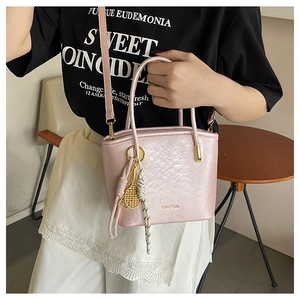 Detail of light pink bucket bag featuring embossed texture and gold tennis racket charm