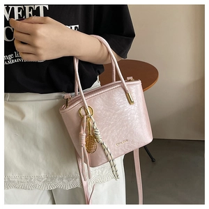 Detailed view of pink textured bucket bag featuring a tennis racket charm and gold hardware