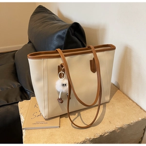 Detail of minimalist beige tote bag with brown trim and cute plush ball charm accessory