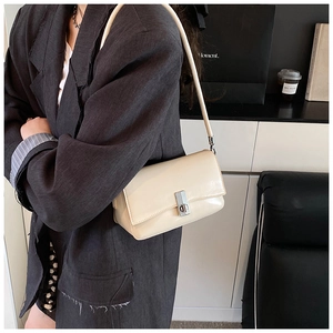 Detail showing creamy faux leather shoulder bag with silver metal lock on a grey suit jacket