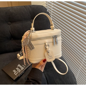 Détail du sac boîte crème texturé avec breloque raquette de tennis et zip argenté