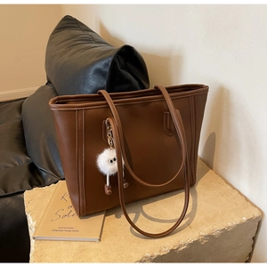 Detail of dark brown faux leather tote bag with plush charm on a textured stone surface