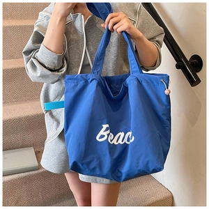 Close-up of blue nylon tote bag showing white Beao lettering and pink adjustment buckle