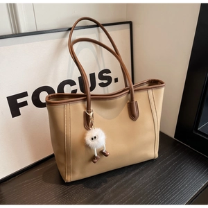Detail view of khaki tote bag with brown handles and a cute white plush doll keychain