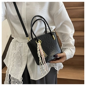 Detail of black textured bucket bag with golden rings and decorative silk scarf