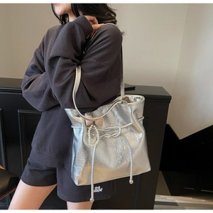 Dettaglio della borsa tote argento metallizzato con nodo a coulisse e ciondolo di perla