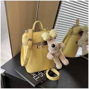 Detail of yellow lychee texture mini bag featuring a cute plush dog charm on a book