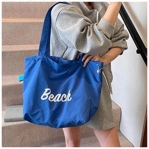 Close-up of bright blue tote bag with white Beach text and side drawstring detail