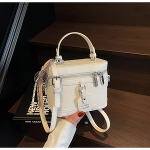 Gros plan du sac boîte en cuir blanc avec poignée, breloque tennis et foulard en soie rayé