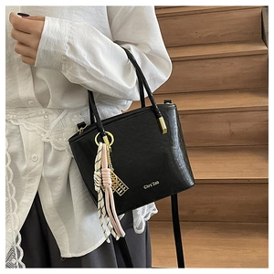 Detail of black PU bucket bag featuring gold brand lettering and elegant fringe pendant