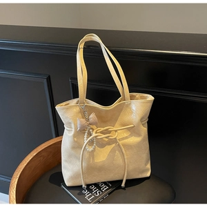 Dettaglio della borsa tote beige in pelle cerata con fiocco a quadri e ciondolo di perle