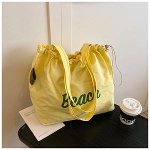 Detail of a yellow canvas tote bag with green Beach print and drawstring closure