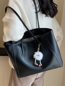 Minimalist black leather tote bag with plush charm shown from a 45-degree angle