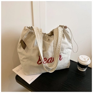 Detail of canvas tote bag showing drawstring closure and red Beach print lettering
