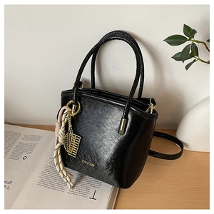 Close-up of black PU leather bucket bag featuring gold brand lettering and metallic charms