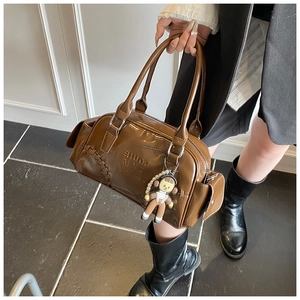 Close-up of brown glossy leather bowling bag with cute doll charm and embossed logo