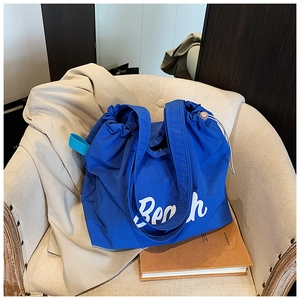 Detail view of a blue nylon drawstring beach tote bag on a beige armchair with letters