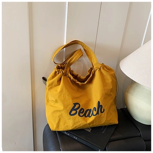 Detail of a bright yellow drawstring tote bag featuring artistic blue Beach print