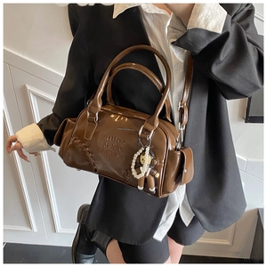 Detail of a brown patent leather bowling bag featuring contrast stitching and a pearl charm