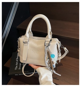 Detailed macro of cream faux leather Boston bag with embossed lettering and colorful charms