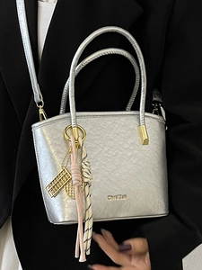Silver metallic bucket bag with dual handles and branding shown on a black suit model