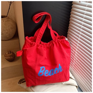 Detail of red canvas tote bag with blue Beach lettering and drawstring closure