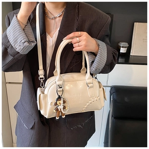 Detail view of cream white patent leather bowling bag with doll pendant and pearl chain