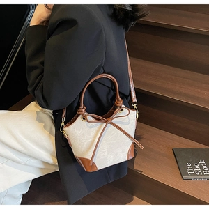 Détail du sac seau en toile montrant la texture tissée, le nœud en cuir et les dorures
