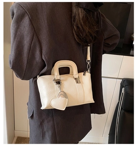 Detail of cream white PU leather square bag featuring a heart pendant and metal buckle