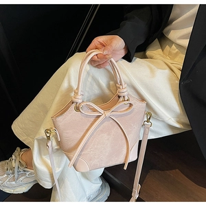 Détail du sac seau rose clair avec un grand nœud décoratif et des éléments en métal doré