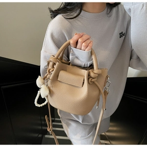Detail of khaki litchi grain leather bucket bag with bow and pearl charms accessory