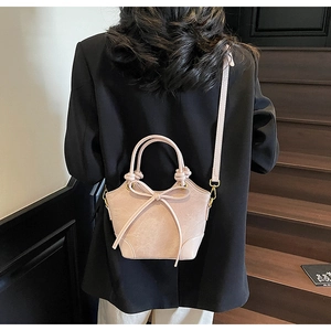 Détail du sac seau rose clair avec nœud et bandoulière sur mannequin dans l'escalier